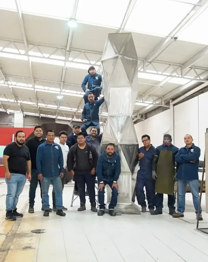 UKMA production team standing beside a large geometric sculpture inside the Mexico workshop
